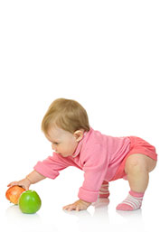 A baby bending over to pick up an apple